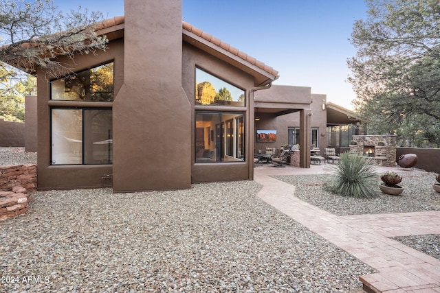 back of house featuring an outdoor stone fireplace, a patio, and stucco siding