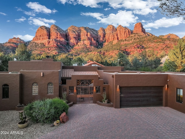 pueblo-style house with decorative driveway, stucco siding, a gate, a mountain view, and a garage