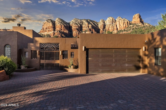 pueblo-style home featuring a garage, a gate, decorative driveway, and stucco siding