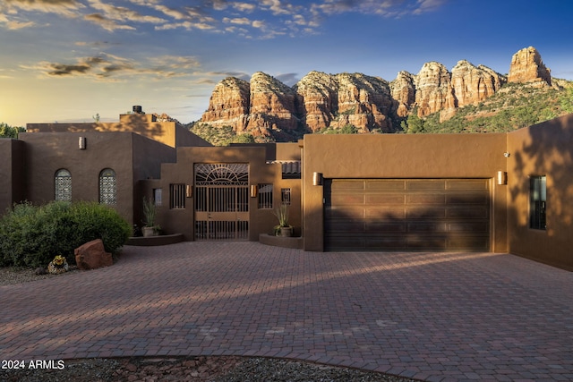 adobe home featuring decorative driveway, a gate, an attached garage, and stucco siding