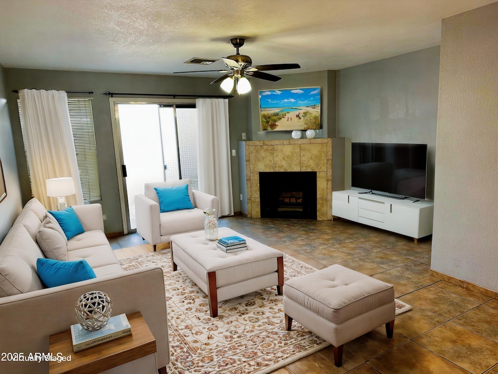 living room with a tiled fireplace, ceiling fan, and a textured ceiling