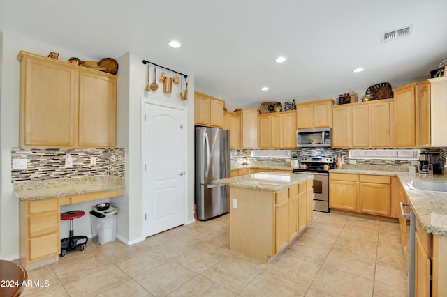 kitchen with stainless steel appliances, a center island, light brown cabinetry, and light stone counters