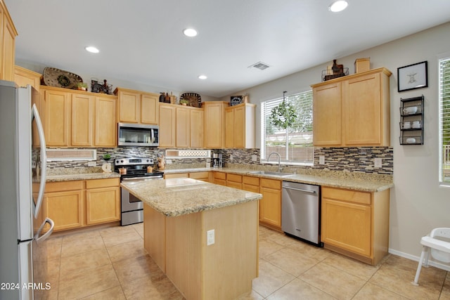 kitchen with stainless steel appliances, light stone countertops, light tile patterned floors, a kitchen island, and sink