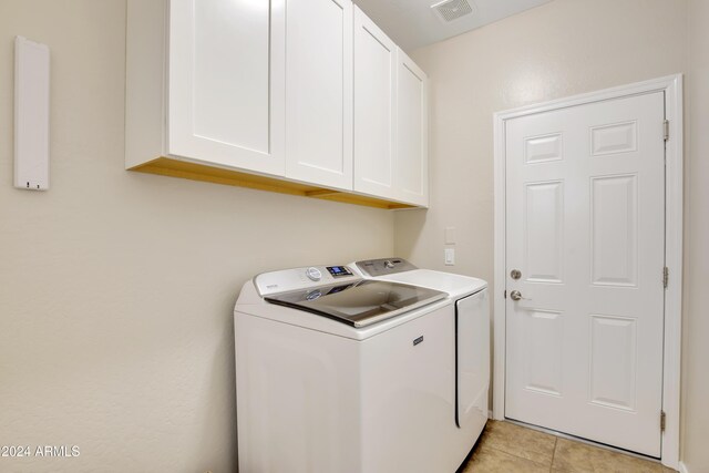 clothes washing area with washing machine and dryer, light tile patterned floors, and cabinets