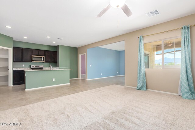 kitchen with electric range oven, dark brown cabinetry, a kitchen island with sink, light carpet, and ceiling fan