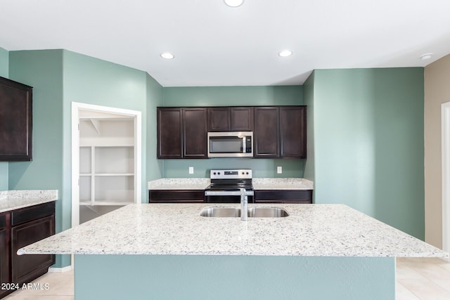 kitchen featuring sink, light stone counters, appliances with stainless steel finishes, light tile patterned floors, and a kitchen island with sink