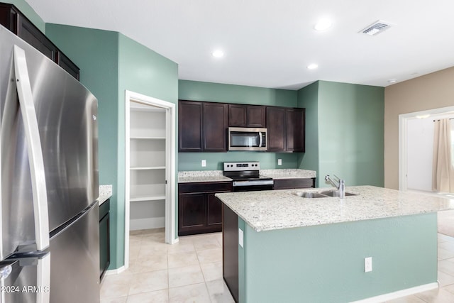 kitchen with dark brown cabinetry, sink, light tile patterned floors, appliances with stainless steel finishes, and a kitchen island with sink