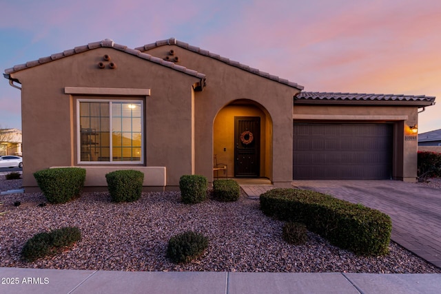 mediterranean / spanish-style home with a tiled roof, decorative driveway, an attached garage, and stucco siding