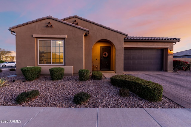 mediterranean / spanish house with a garage, a tiled roof, decorative driveway, and stucco siding