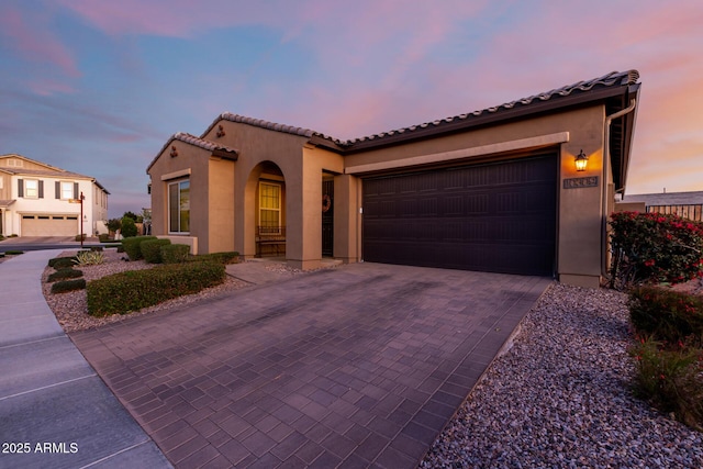 mediterranean / spanish house with decorative driveway, an attached garage, a tile roof, and stucco siding