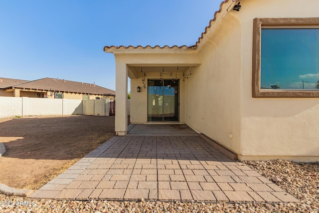 entrance to property with a patio area, fence, and stucco siding