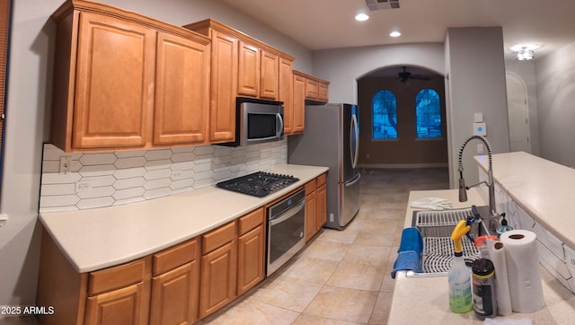 kitchen featuring arched walkways, stainless steel appliances, light countertops, backsplash, and a ceiling fan