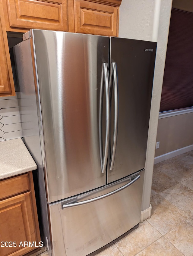 kitchen featuring baseboards, brown cabinetry, light countertops, and freestanding refrigerator