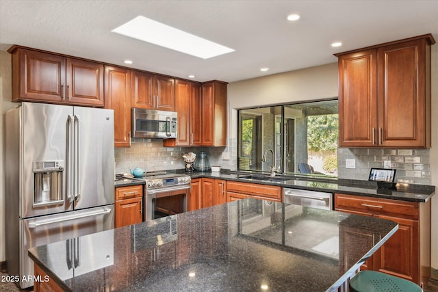 kitchen featuring dark stone countertops, sink, a skylight, and appliances with stainless steel finishes