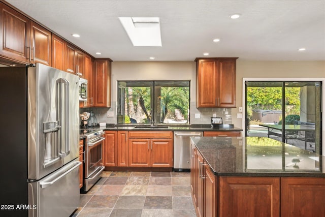 kitchen with dark stone countertops, stainless steel appliances, a skylight, and backsplash