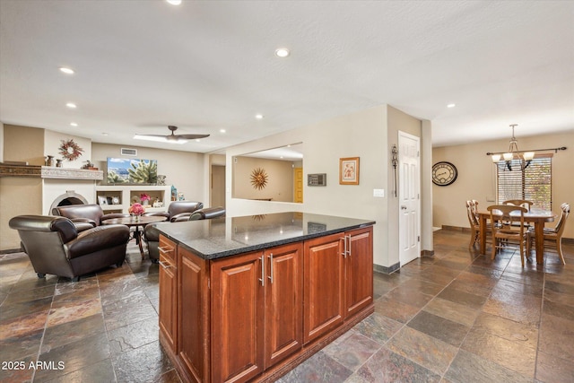 kitchen featuring a center island, ceiling fan with notable chandelier, dark stone counters, and decorative light fixtures