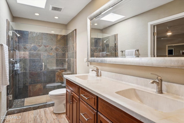 bathroom featuring a skylight, hardwood / wood-style flooring, vanity, toilet, and a shower with door