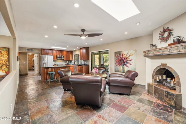 living room featuring ceiling fan, a fireplace, and a skylight