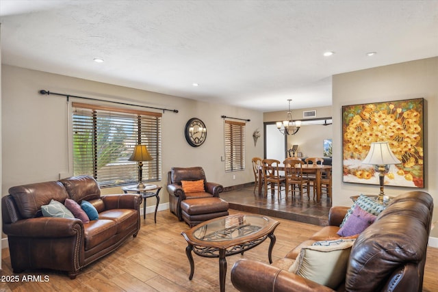 living room with a textured ceiling, a chandelier, and light wood-type flooring