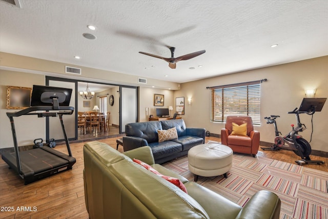 living room with ceiling fan with notable chandelier, light hardwood / wood-style floors, and a textured ceiling