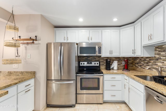 kitchen with white cabinetry, stainless steel appliances, tasteful backsplash, light stone counters, and sink