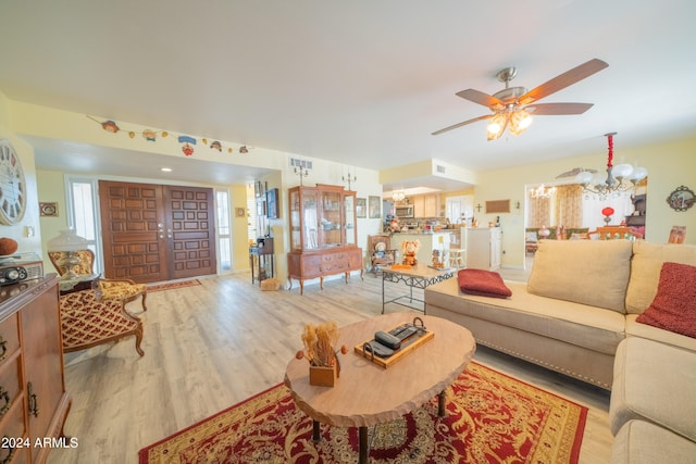 living room with ceiling fan with notable chandelier and light hardwood / wood-style floors