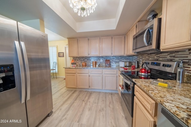 kitchen featuring appliances with stainless steel finishes, backsplash, a tray ceiling, a notable chandelier, and light hardwood / wood-style floors