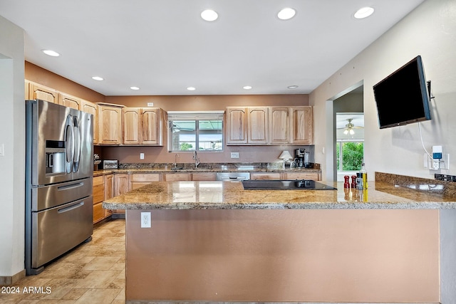 kitchen with light stone countertops, stainless steel appliances, light brown cabinetry, sink, and kitchen peninsula