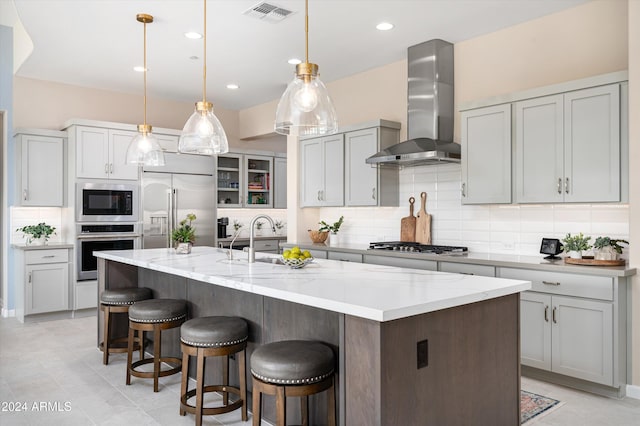 kitchen with built in appliances, decorative light fixtures, a kitchen island with sink, and wall chimney exhaust hood