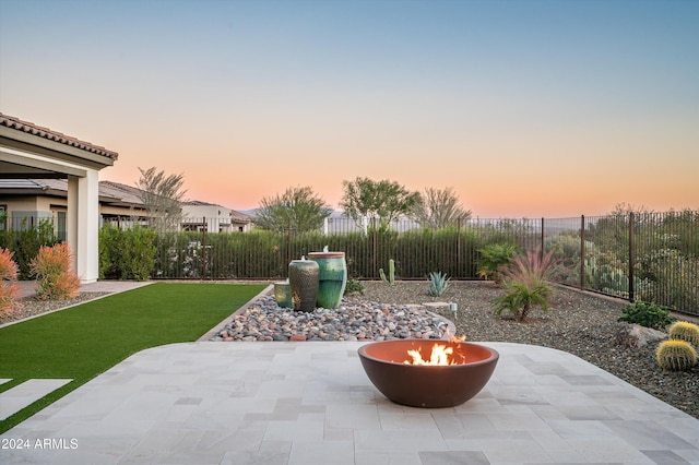 patio terrace at dusk featuring a lawn and a fire pit