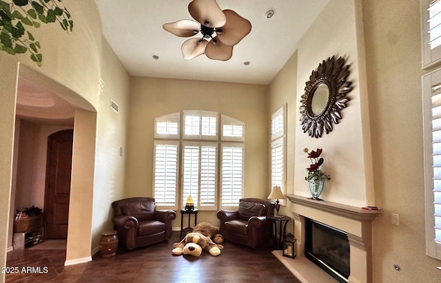 living area featuring a ceiling fan, visible vents, wood finished floors, baseboards, and a large fireplace