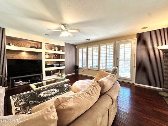 living area featuring built in shelves, a ceiling fan, wood finished floors, baseboards, and a textured ceiling