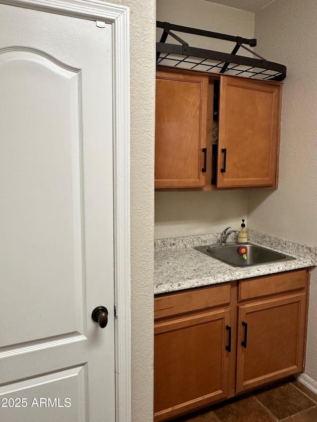 kitchen with a sink, brown cabinets, dark tile patterned flooring, and light countertops