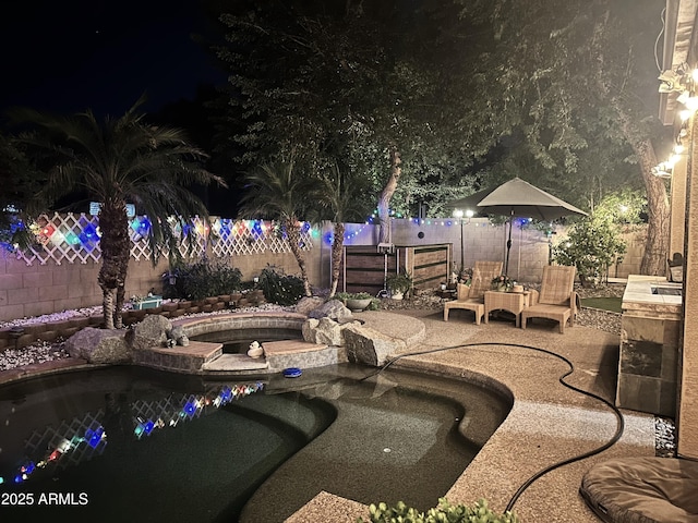 pool at night with a patio, an in ground hot tub, and a fenced backyard