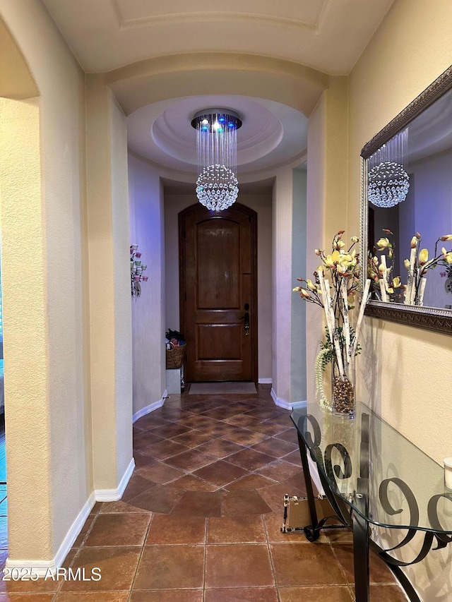 hallway with arched walkways, baseboards, and a tray ceiling