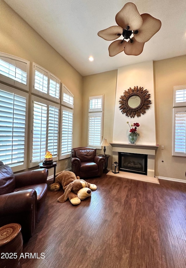 living room with a glass covered fireplace, baseboards, wood finished floors, and a ceiling fan