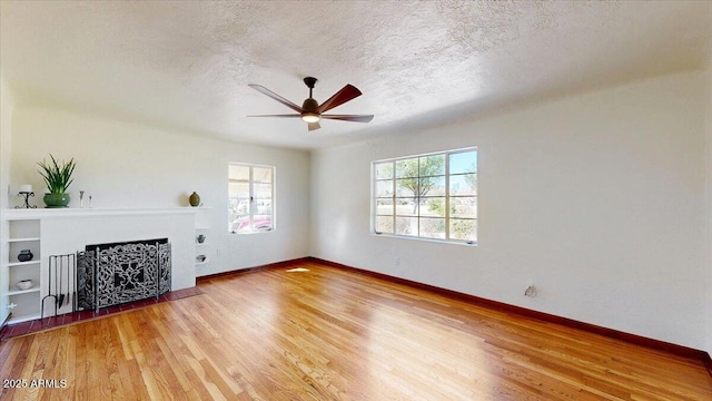 unfurnished living room featuring a fireplace with flush hearth, a textured ceiling, wood finished floors, and baseboards