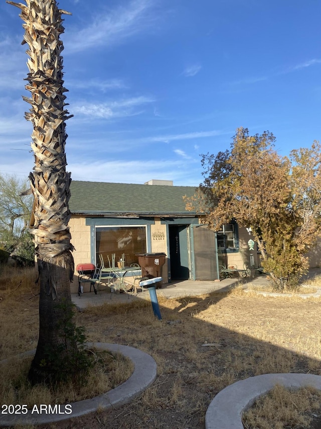 back of property featuring a patio area, a shingled roof, and concrete block siding