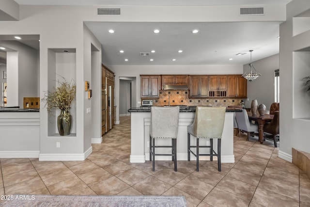 kitchen with tasteful backsplash, visible vents, under cabinet range hood, a chandelier, and a breakfast bar