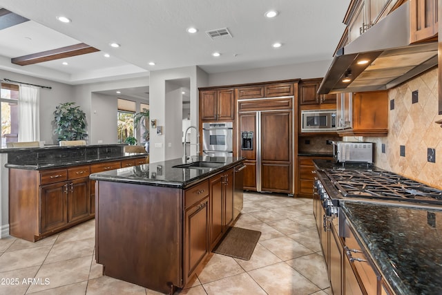 kitchen with visible vents, under cabinet range hood, built in appliances, an island with sink, and a sink