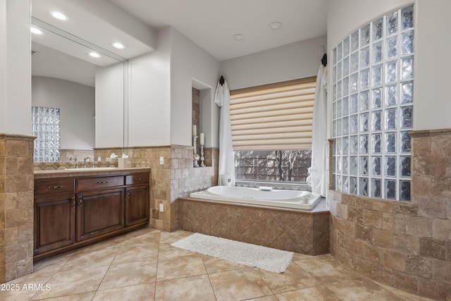 full bath featuring tile patterned flooring, tile walls, a garden tub, wainscoting, and vanity