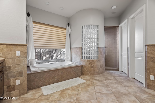 full bath with a wainscoted wall, tiled shower, tile walls, and a bath