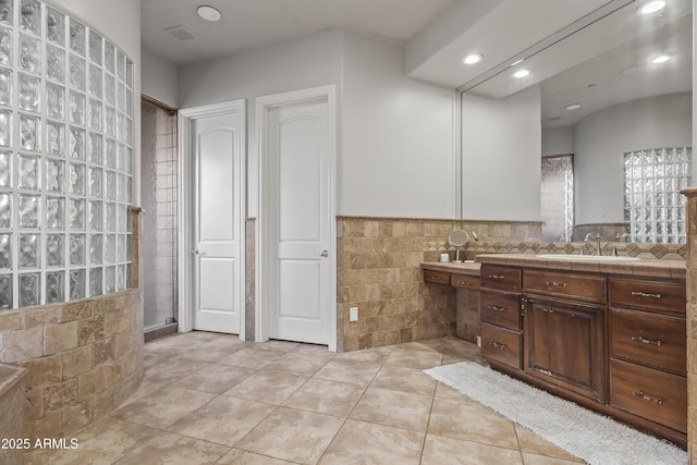 bathroom with visible vents, tile walls, tile patterned flooring, tiled shower, and vanity