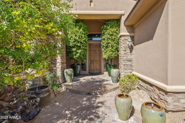 doorway to property featuring a patio area, stone siding, and stucco siding