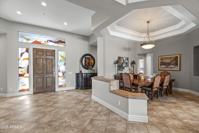 entrance foyer with light tile patterned floors, a tray ceiling, and baseboards