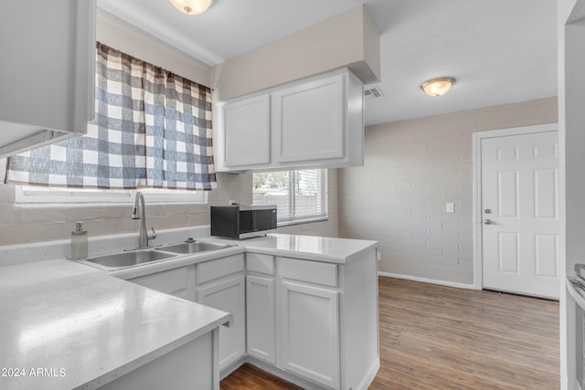 kitchen with kitchen peninsula, sink, white cabinetry, light hardwood / wood-style flooring, and brick wall