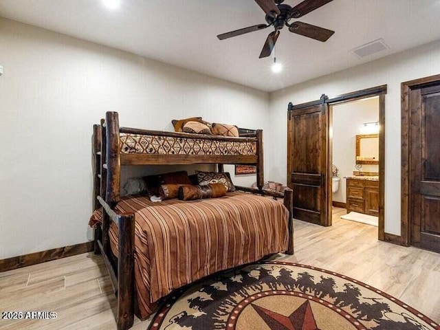 bedroom featuring ceiling fan, ensuite bathroom, light hardwood / wood-style floors, and a barn door