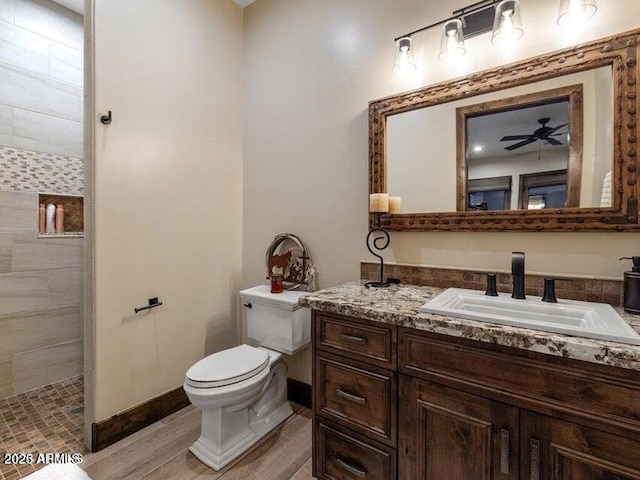 bathroom featuring toilet, hardwood / wood-style flooring, ceiling fan, tiled shower, and vanity