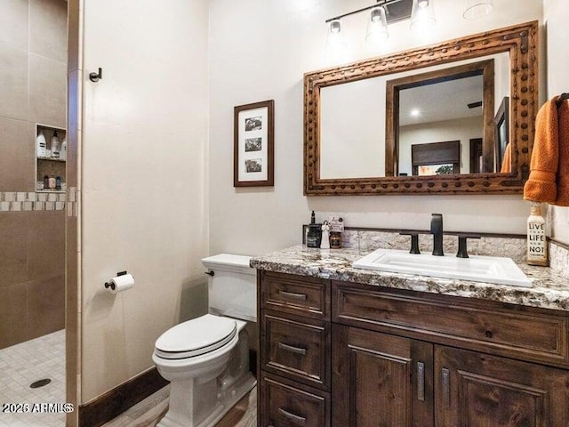 bathroom featuring toilet, tiled shower, and vanity