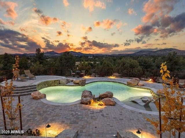 pool at dusk featuring a mountain view and a patio